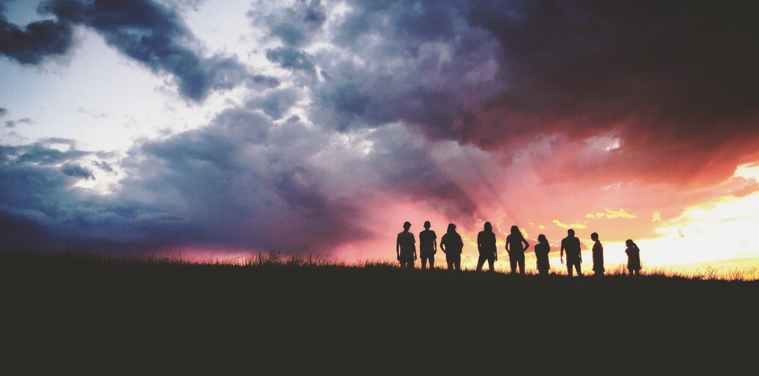 A group of people in silhouette with an orange sunset in the background