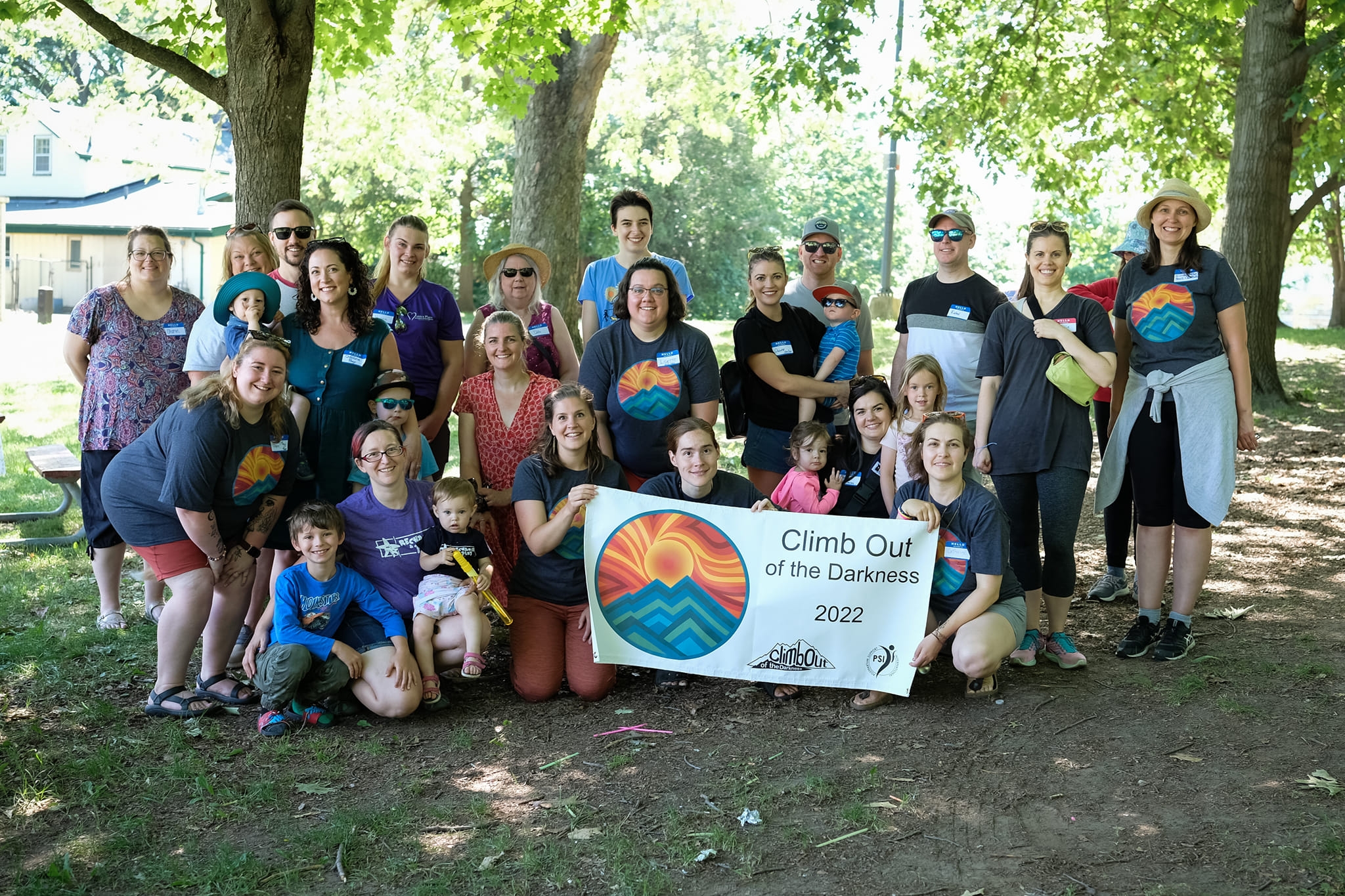 A gathering of people, ranging from one year to grey hair, at the front, a few are holding a banner that has the 10th anniversary climb logo and says "Climb out of the darkness 2022" on it.