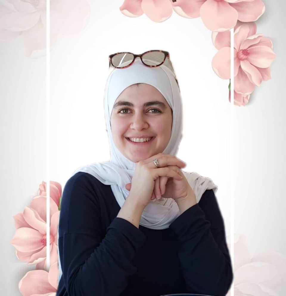 Suzan is a white muslim woman wearing a white hijab with glasses on top of her head. Her hands are folded in front of her under her chin. 