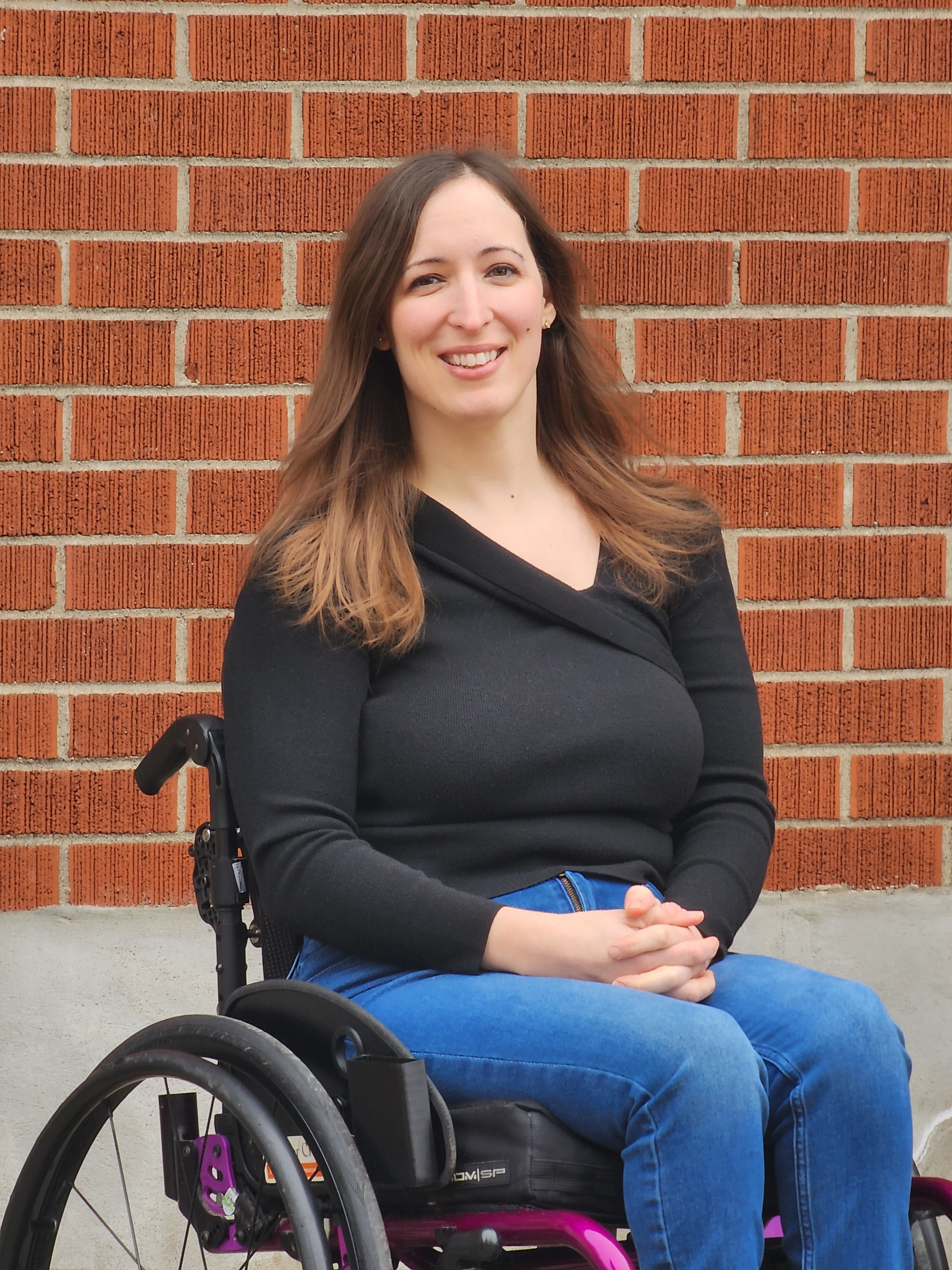 Leanne is a white woman with light brown hair, she is wearing a black shirt and jeans. She sits in a wheelchair.