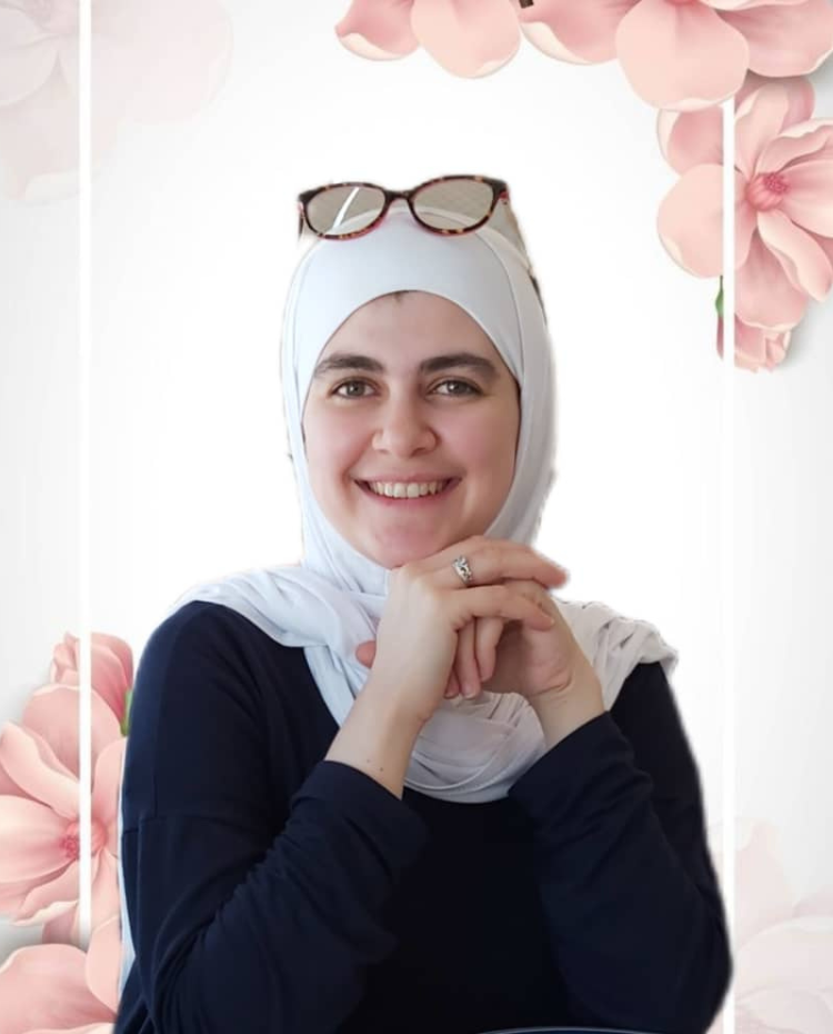 Suzan is a woman wearing a white Hijab, her hands are folded under her chin and there are glasses on top of her head. There are pink flowers behind her.